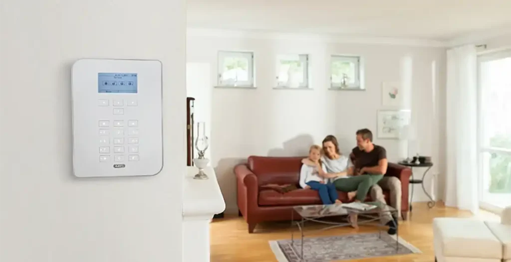 Wandmontierte ABUS Alarmanlage in hellem Wohnraum mit sitzender Familie im Hintergrund