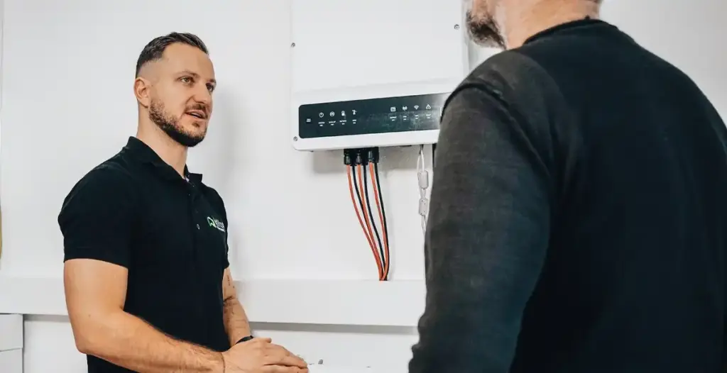 Geschäftsführer Markus Zink erklärt einem Kunden die Funktionen eines Stromspeichers an der Wand bei einer Beratung