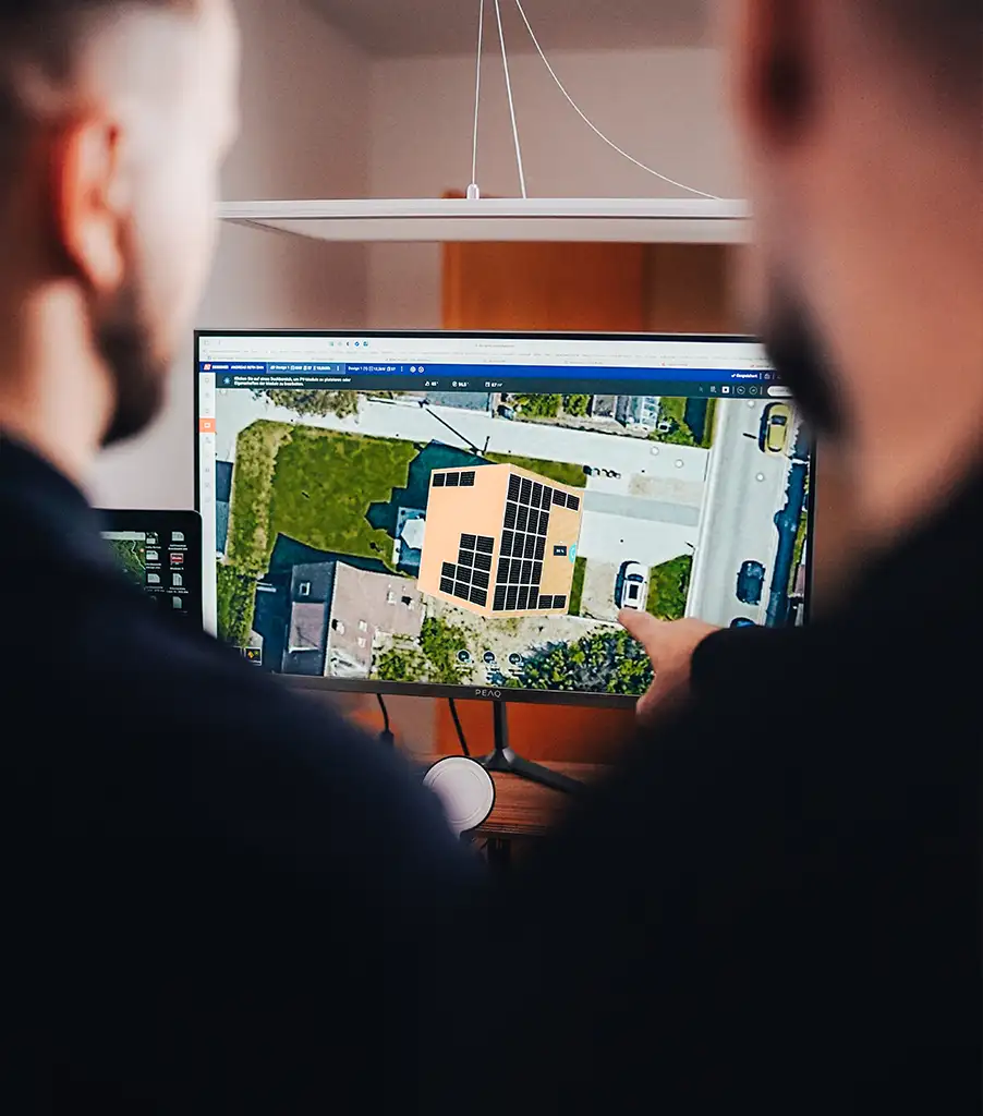 Zwei Personen betrachten eine Luftaufnahme eines Hauses mit Photovoltaikanlage auf dem Dach auf einem Computerbildschirm, Planungswerkzeuge für die Installation sind sichtbar.