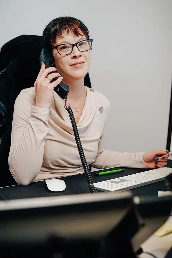 Karoline, eine engagierte Mitarbeiterin, führt ein Kundengespräch am Telefon. Ihre freundliche Haltung und ihr aufmerksamer Blick spiegeln die kundenfreundliche Atmosphäre bei ihrer Arbeit wider.