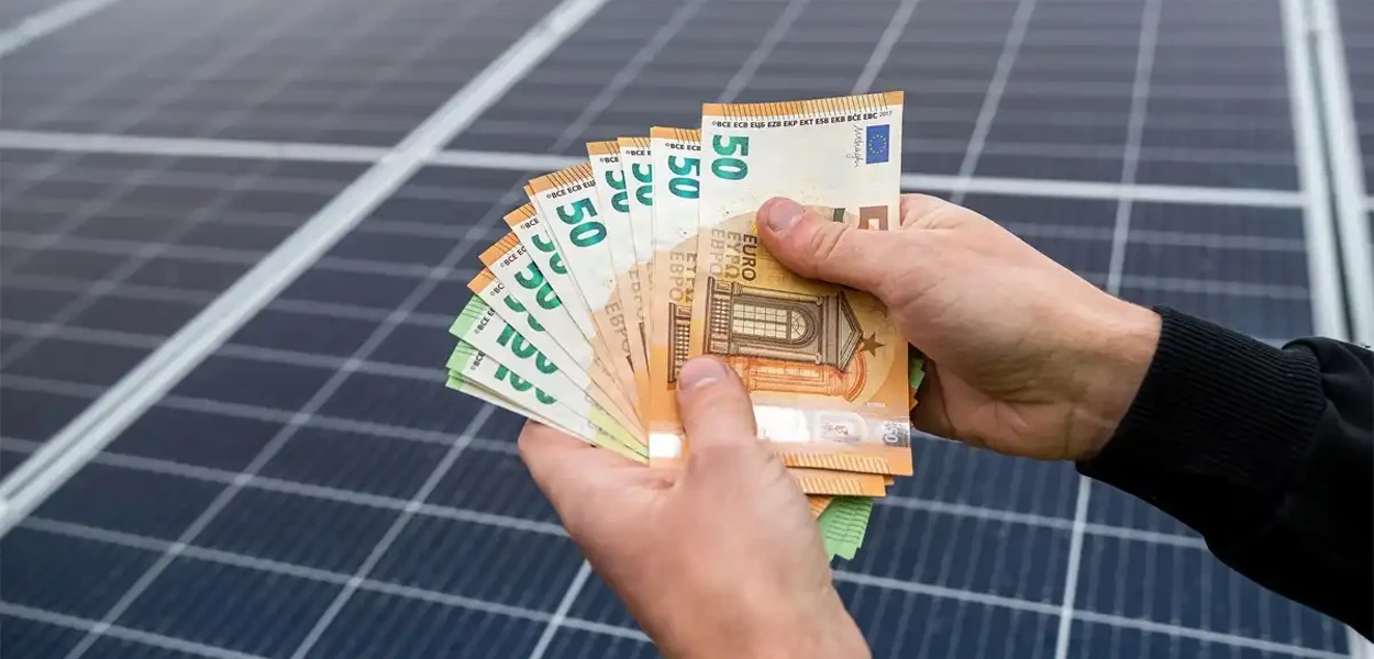 Geldscheine vor den Platten einer Photovoltaikanlage. Thematisch passend zu den Förderung für Solaranlagen in 2026