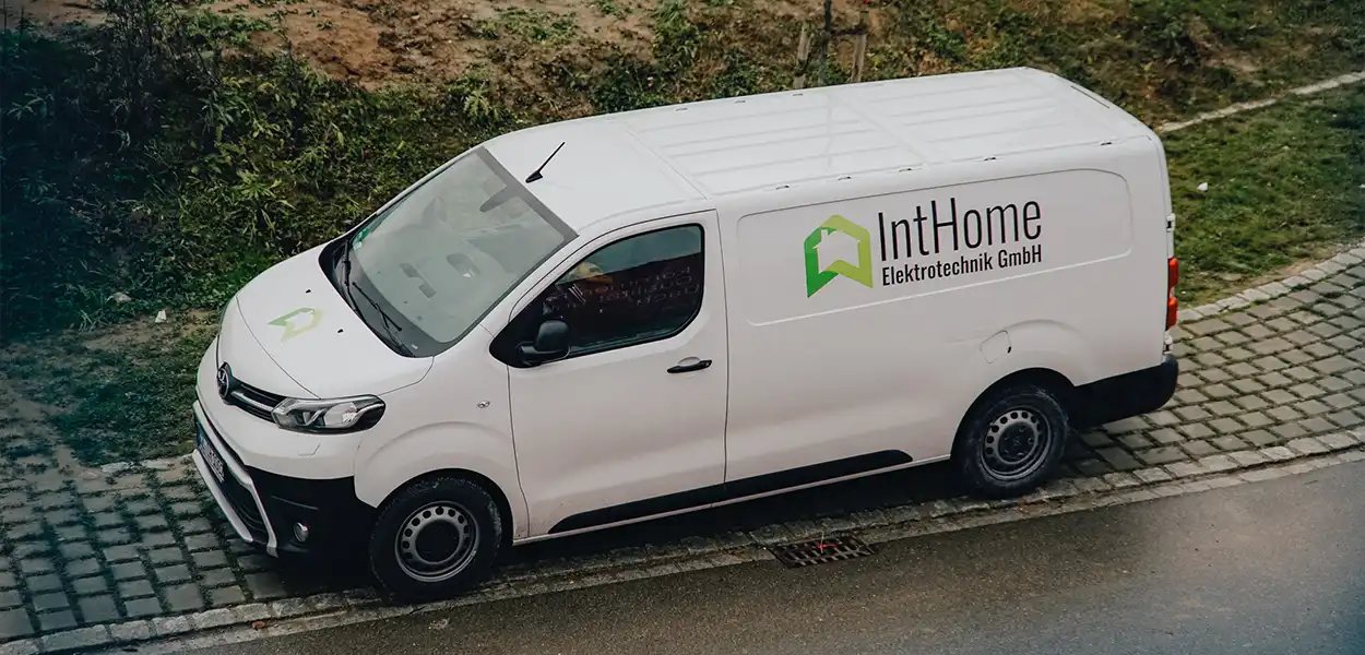 Weißer Lieferwagen der Firma IntHome Elektrotechnik GmbH auf gepflasterter Straße neben einer Grünfläche, Firmenlogo mit grünem Haus-Symbol und schwarzem Schriftzug