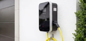 Moderne Wallbox mit gelbem Ladekabel an weißer Hauswand, Ladestation für Elektroautos in Mehrfamilienhaus